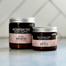 Two different sized jars of Mountain Time Soap & Supply Better Body Butter on a light surface with a tiled wall background.