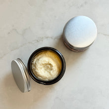 Open jar of body butter with a lid on a marble surface