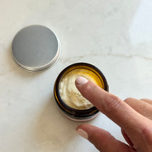 Finger applying cream from an open jar on a marble surface