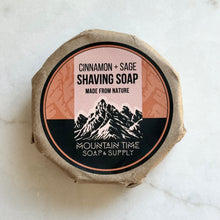 Cinnamon and sage shaving soap packaging with mountain design on a white marble background